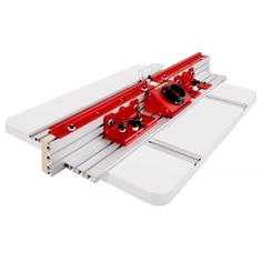 a red and white table sawing machine on top of a white board with two pieces of wood