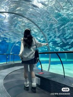 a woman standing in front of an aquarium looking at fish