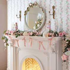 a white fireplace with pink flowers on the mantle and a mirror above it that is decorated with greenery