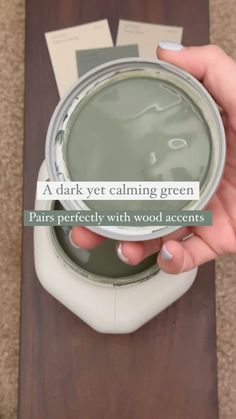 a person holding a paint can with the words, a dark yet calming green pairs perfectly with wood accents