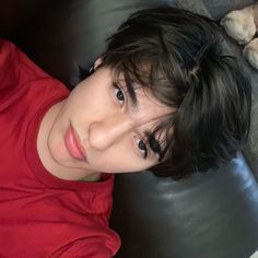 a young boy sitting on top of a couch next to a teddy bear and wearing a red shirt