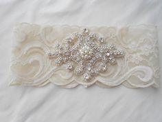 a white garter with pearls and bows on it's side, sitting on a bed