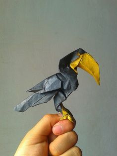 a hand holding a small bird made out of origami paper in the shape of a toucan