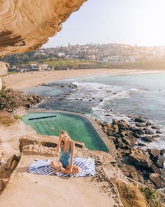 a woman sitting on top of a beach next to the ocean with a towel around her