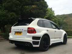 the rear end of a white car parked in a parking lot next to some trees