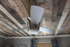 a ceiling fan mounted to the side of a wooden ceiling in a room with plaid curtains