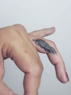 a person's hand with a small feather tattoo on the middle finger and fingers