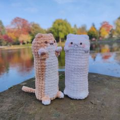 three crocheted cats standing next to each other on top of a rock near water