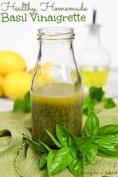 basil vinaigrette in a glass bottle with fresh basil leaves and lemons behind it