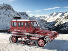 a red vehicle that is sitting in the snow with mountains in the backgroud