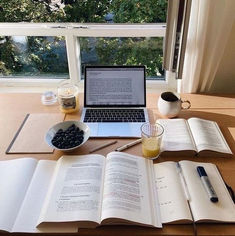 an open book sitting on top of a wooden table next to a laptop computer and cup of coffee