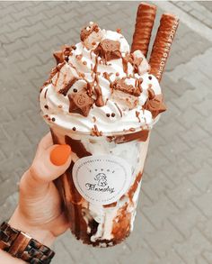 a person holding up a chocolate milkshake with whipped cream and pretzels on top