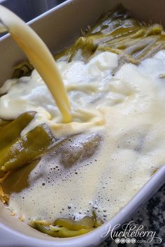 a person pours sauce into a casserole dish with green beans and asparagus