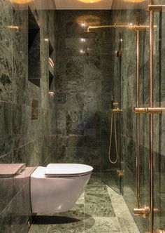 a bathroom with green marble walls and flooring, along with a white toilet in the middle