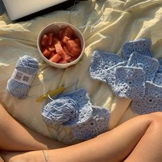 a woman laying on top of a bed next to crocheted items and a bowl of watermelon