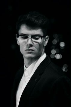 a man wearing glasses and a suit in front of a black background with boke lights