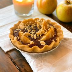 an apple pie sitting on top of a wooden table next to two apples and a candle