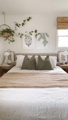 a bed with white linens and pillows in a bedroom next to two plants on the wall