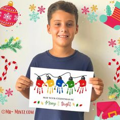 a young boy holding up a card with christmas lights on it and decorations around him