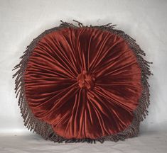 a red pillow with fringes on it sitting on a white surface in front of a wall