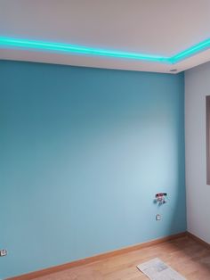 an empty room with blue walls and wood flooring is lit by neon lights on the ceiling