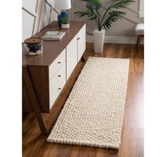 a white rug on top of a wooden floor next to a lamp and plant in a vase