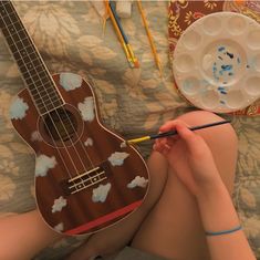 a person sitting on a bed with a guitar and paintbrush in their hand,