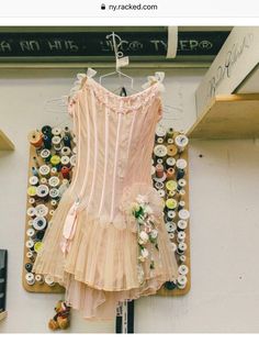 a pink corset is hanging on a wall with buttons and ribbons around it