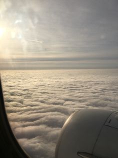 the view out an airplane window shows clouds below and in the distance is a plane wing