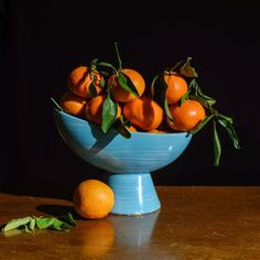 a blue bowl filled with oranges sitting on top of a wooden table next to leaves