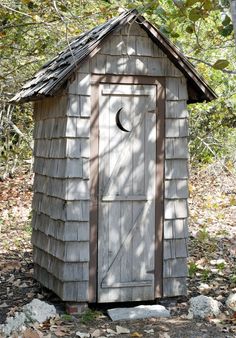 an outhouse in the woods with a half moon on it's roof and door