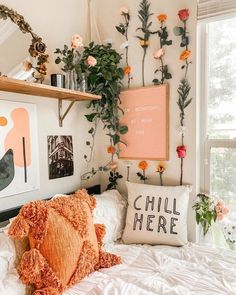 a white bed topped with lots of pillows next to a wall filled with pictures and plants