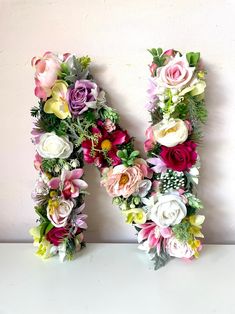 the letter h is made up of flowers and greenery in front of a white wall