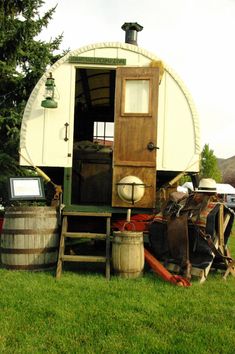 a horse trailer is parked in the grass next to barrels and buckets on the ground