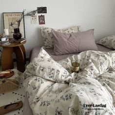 an unmade bed in a bedroom with white walls and flooring, along with various items on the table