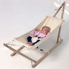 a baby is laying in a hammock on a white background with a wooden frame