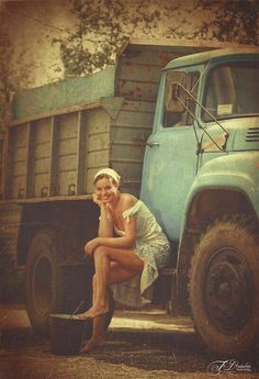 a woman sitting on the back of a blue truck next to a dumptruck