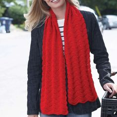 a woman wearing a red scarf is holding a black suitcase and smiling at the camera