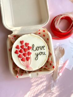 a heart shaped cookie with the words love you on it in a box next to some spools of thread