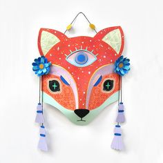 a red fox mask with blue flowers on it's head and eyes are hanging from the wall