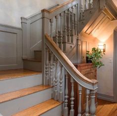 a staircase with wooden handrails and white painted walls in a home, next to a potted plant