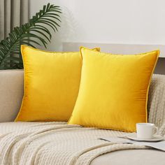 two yellow pillows sitting on top of a couch next to a cup and saucer