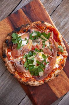 a pizza sitting on top of a wooden cutting board covered in toppings and veggies