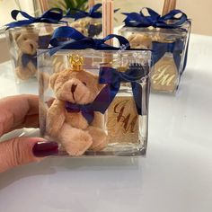 a small teddy bear in a clear box with blue ribbon around it's neck