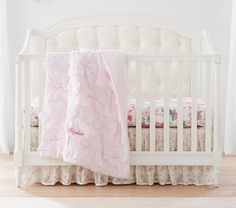 a white crib with a pink blanket on top of it and floral bedding