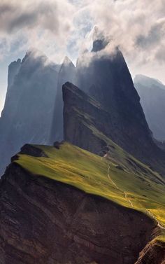 the mountains are covered with green grass and clouds in the distance is a road running between them