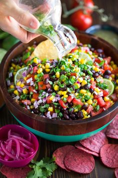 a person is pouring salsa into a bowl with tortilla chips and cilantro