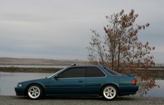 a blue car parked next to a body of water with a tree in the background