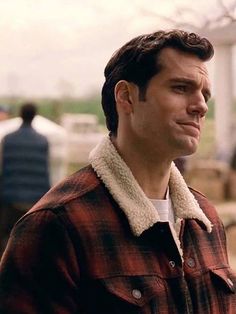 a man wearing a red and black plaid jacket smiling at the camera while standing in front of a building