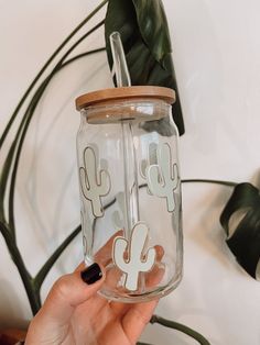 a person holding up a glass jar with stickers on it and a plant in the background